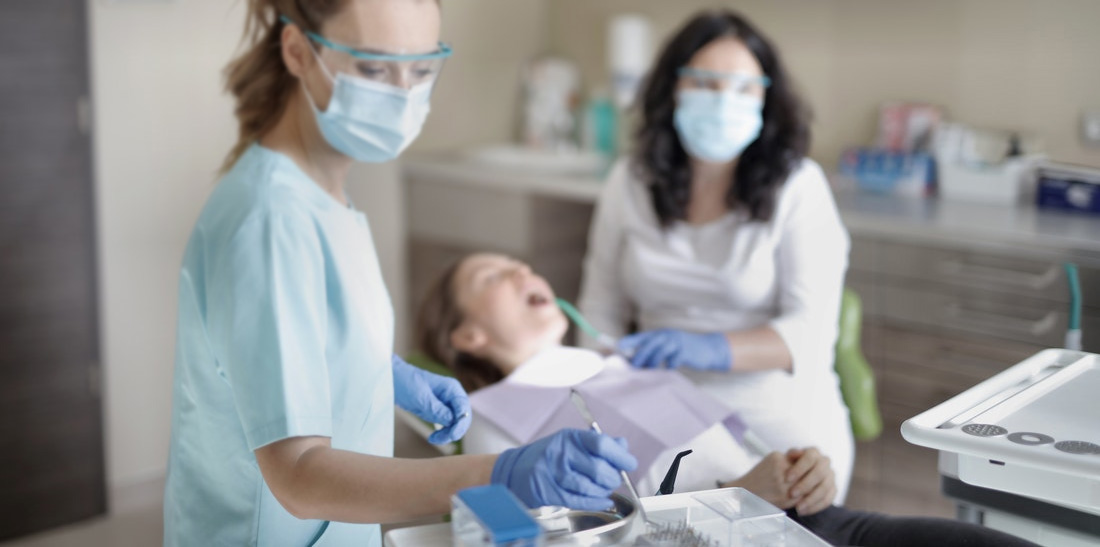 A woman sitting in a dentist chair with while two dentist involved in the procedure.