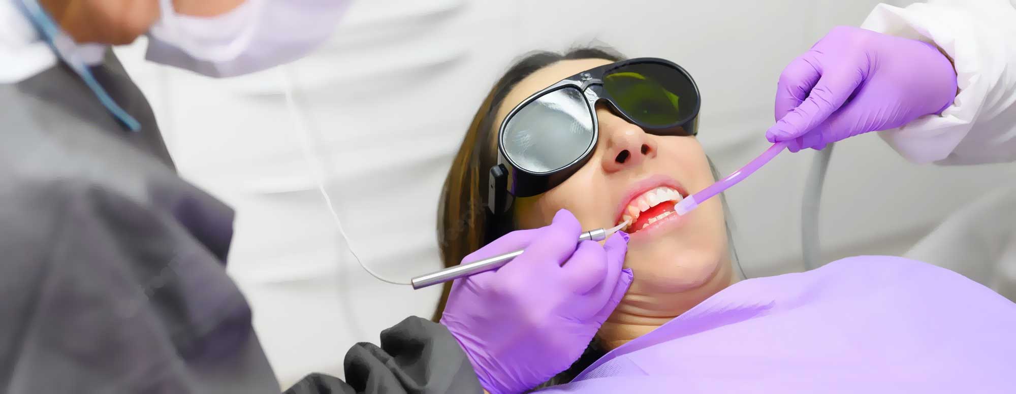 A dentist cleaning a woman's teeth,with dental laser