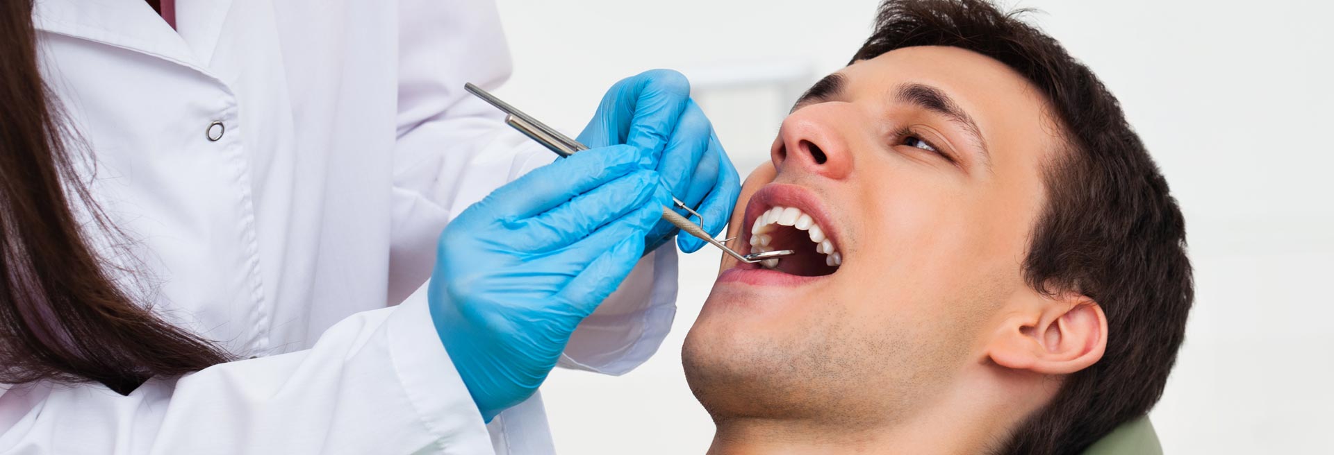 A man sitting in a dentist's chair while the dentist examines his teeth for root canal treatment