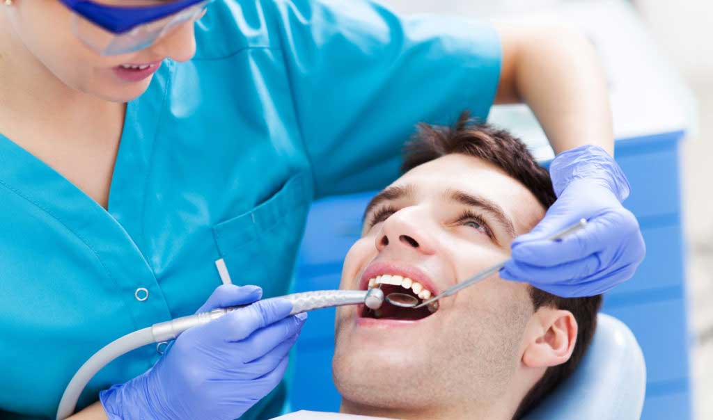 A dentist cleaning a man's teeth, ensuring oral hygiene and maintaining dental health.