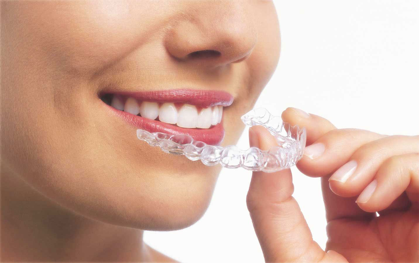 A woman with a pleasant expression holds Invisible Aligners putting in her mouth, showcasing a smile.
          